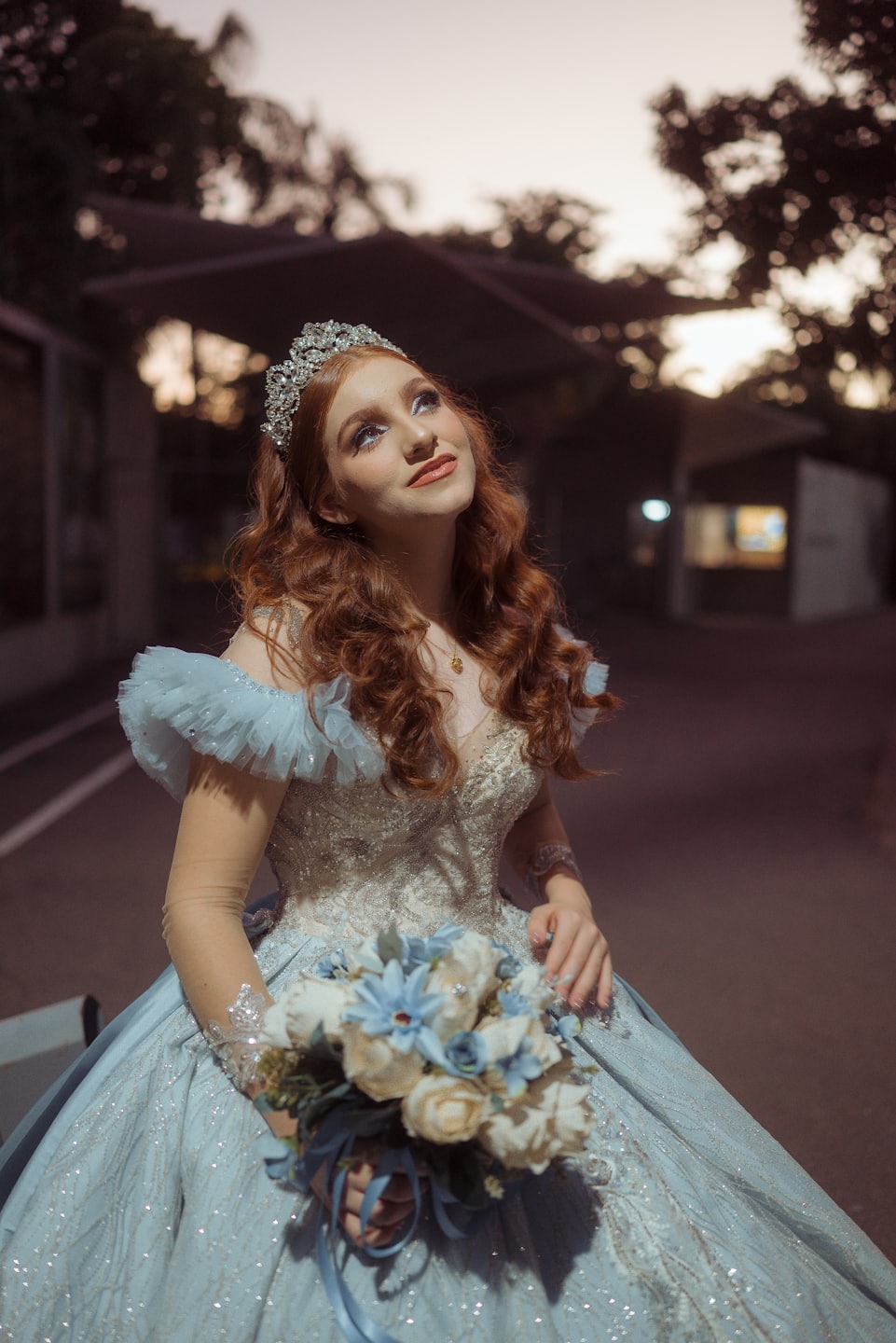 Mujer con vestido y tiara sostiene un ramo al aire libre.