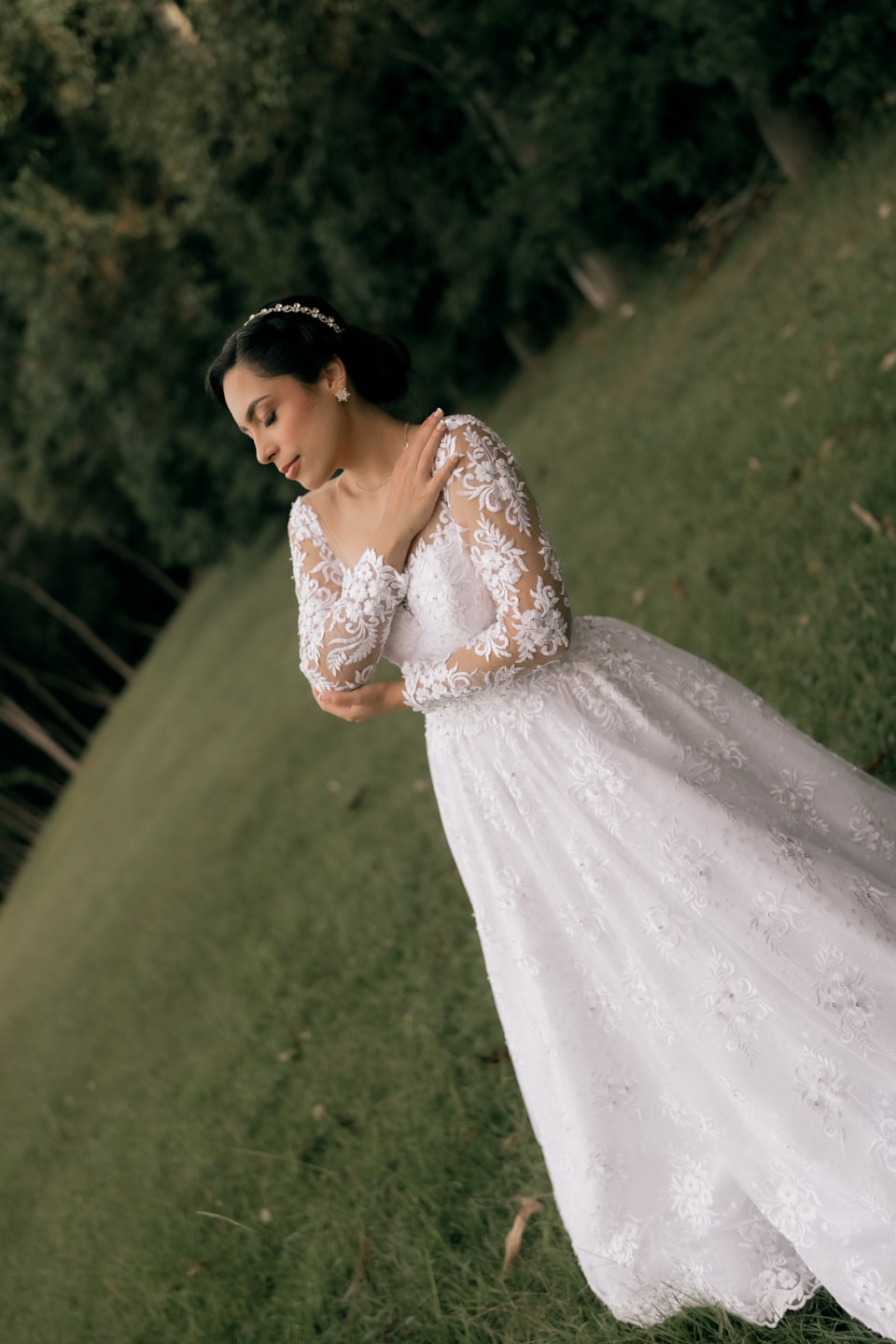 Novia con vestido blanco de encaje de pie en una colina verde.